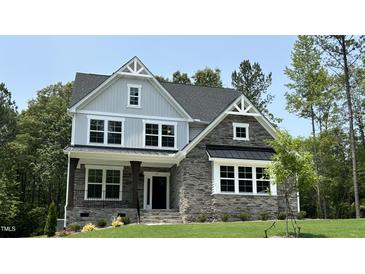 Charming two-story home with stone accents, covered porch, and a well-manicured lawn surrounded by lush trees at 684 Magnolia Acres Ln, Fuquay Varina, NC 27526