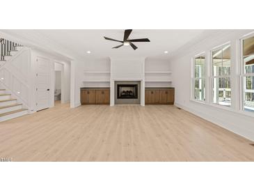 Bright living room featuring a fireplace, built-in shelving, ceiling fan and large windows at 617 Darian Woods Dr, Holly Springs, NC 27540