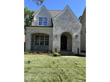 Charming home featuring a light brick facade, arched entryway, manicured lawn, and beautiful architectural details at 3302.5 Hall Pl, Raleigh, NC 27607