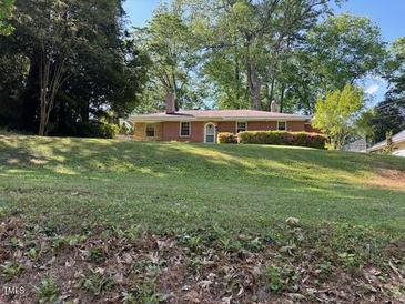 Charming red brick home with a well-manicured lawn and mature trees, nestled on a sunny, grassy knoll at 2705 Royster St, Raleigh, NC 27608