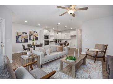 Open-concept living room with modern furnishings and wood flooring leading to the contemporary kitchen at 3856 Well Fleet Drive, Fuquay Varina, NC 27526