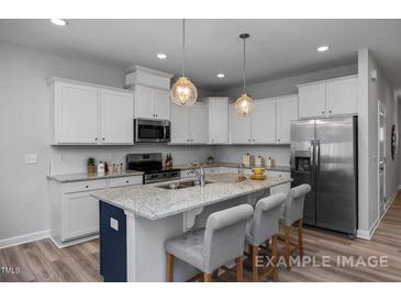 Bright kitchen features white cabinetry, stainless appliances, granite countertops, and island with seating at 3930 Well Fleet Drive, Fuquay Varina, NC 27526