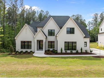 A beautiful two-story, white brick home with dark trim surrounded by a lush green lawn and mature trees at 7813 Ailesbury Rd, Wake Forest, NC 27587