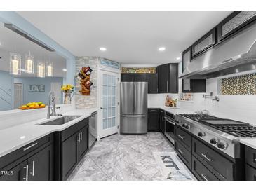 Modern kitchen features stainless steel appliances, black cabinets and a view to the living room at 5705 Katha Dr, Holly Springs, NC 27540