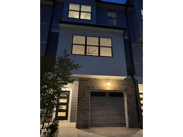 Modern townhome with a gray garage door and brick accents, illuminated by an outdoor light fixture at 702 Portia Way, Homesite 16, Morrisville, NC 27560