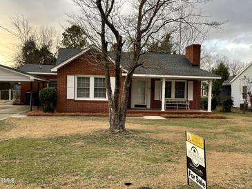 Brick ranch home with covered porch and mature trees. For Sale sign in front yard at 209 N Watauga Ave, Dunn, NC 28334
