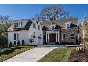 A charming two-story home with stone and white brick exterior, a three-car garage, and a manicured lawn at 1307 Mayfair Rd, Raleigh, NC 27608