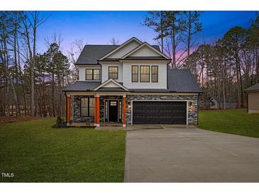 Two-story house with gray stone and white siding, a black garage door, and a covered porch at 99 Prairie Dog Dr, Louisburg, NC 27549