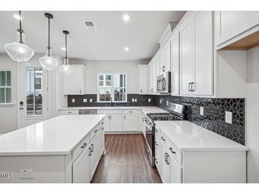 Modern kitchen featuring white cabinets, a kitchen island, stainless steel appliances, and stylish backsplash at 602 Hillfarm Dr, Wake Forest, NC 27587