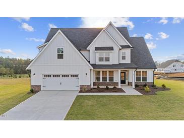 Two-story farmhouse-style home with white siding, brick accents, and a three-car garage at 132 Tennyson Dr, Garner, NC 27529