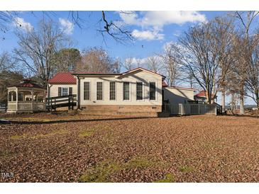 Beige home with a red metal roof, a brick base, and an adjacent gazebo and deck on a sunny day at 253 Ronald Tharrington Rd, Louisburg, NC 27549