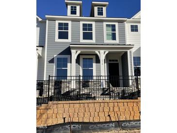 Charming gray two-story home boasts a welcoming front porch and elegant black wrought iron fence at 498 Traditions Grande Blvd # 23, Wake Forest, NC 27587