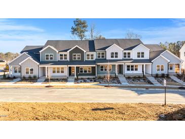 New construction townhomes with modern farmhouse style exteriors, paved sidewalks and young trees under a clear blue sky at 3935 Willow Gate Way, Knightdale, NC 27604