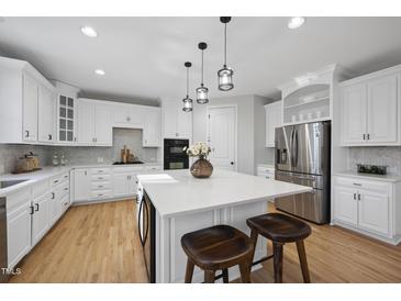 Bright, white kitchen features an island with seating, stainless steel appliances, and hardwood floors at 109 Aspenridge Dr, Holly Springs, NC 27540
