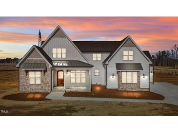 Two-story farmhouse with stone accents and metal roof, beautifully lit at sunset at 4912 Hidden Pasture Way, Zebulon, NC 27597