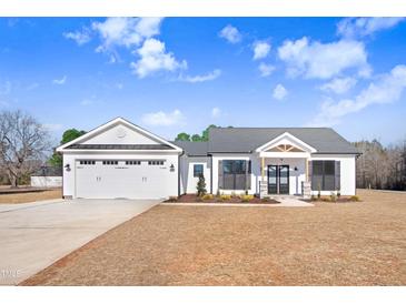 White farmhouse exterior with a three-car garage and a covered front porch at 1647 Old Dam Rd, Kenly, NC 27542