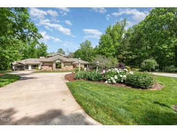 Beautiful home with a circular driveway and a lush, landscaped front yard with various plants and flowers at 12044 Iredell, Chapel Hill, NC 27517