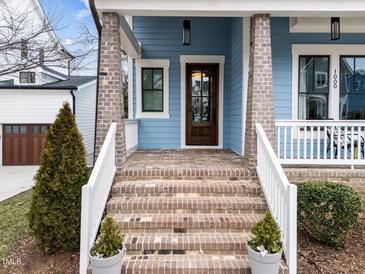 Inviting front porch featuring brick steps, wood door, blue siding, and white railings offers a warm welcome at 1000 Norris St, Raleigh, NC 27604