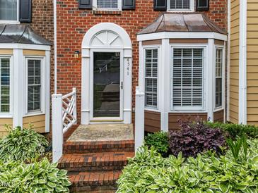 Charming brick townhome featuring a decorative front door, copper bay window, and beautiful landscaping at 4541 Hershey Ct, Raleigh, NC 27613