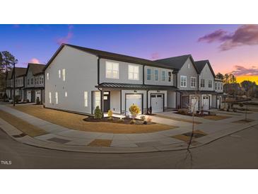 Modern townhome exterior featuring gray siding, white garage doors, and manicured landscaping at sunset at 612 Marshskip Way, Rolesville, NC 27587