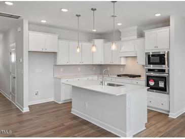 Modern kitchen features white cabinets, stainless steel appliances, and a large island with pendant lighting at 3854 Well Fleet Drive, Fuquay Varina, NC 27526
