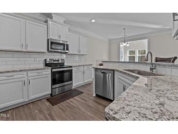 Bright kitchen boasts stainless appliances, granite countertops, white cabinetry, and wood flooring at 25 Bourne Dr, Franklinton, NC 27525