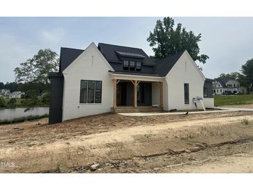 Newly built home with a white painted brick facade, dark roof, and wood porch posts, creating a modern farmhouse appeal at 395 Meadow Walk Dr, Fuquay Varina, NC 27526