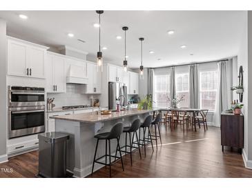 Bright kitchen boasts white cabinets, stainless steel appliances, island seating and an adjacent dining area at 1014 Falling Rock Pl, Durham, NC 27703