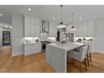 Modern white kitchen featuring a large center island, stainless steel appliances, and hardwood floors at 809 Tower St, Raleigh, NC 27607