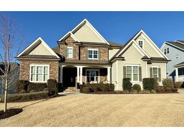 Inviting two-story home featuring a stone facade, covered porch, manicured lawn, and elegant architectural details at 113 Hardy Oaks Way, Holly Springs, NC 27540