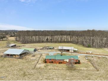 Sprawling property featuring a brick home, multiple outbuildings, fenced acreage, and mature trees at 9550 Silk Hope Liberty Rd, Siler City, NC 27344