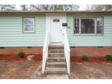 Inviting home with a brick foundation, painted pale green siding, and front door flanked by mulched landscaping at 809 S Plum St, Durham, NC 27701