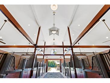 Stunning barn interior with brick flooring, wood beams, and stalls with metal gates and wood paneling at 1018 Terrell Woods Ln, Chapel Hill, NC 27516