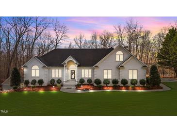 Beautifully landscaped white brick home featuring a manicured lawn, stylish entrance and accent lighting at 1002 Pleasant Dr, Mebane, NC 27302