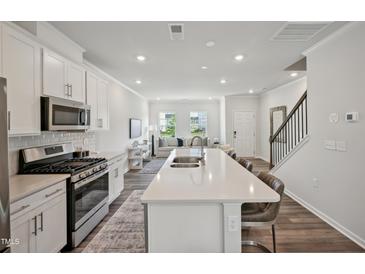 Modern kitchen features stainless steel appliances, white cabinets and an island open to the living room at 687 Mirkwood, Apex, NC 27523