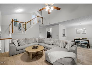 Open-concept living room with a large sectional sofa, hardwood floors, and a staircase at 401 Oak Hollow Ct, Raleigh, NC 27613