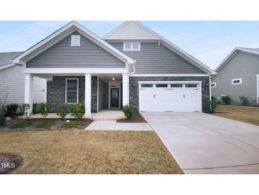 Charming home exterior with stone accents, a two-car garage, covered porch, and landscaped front yard at 475 Bramble Ln, Clayton, NC 27527