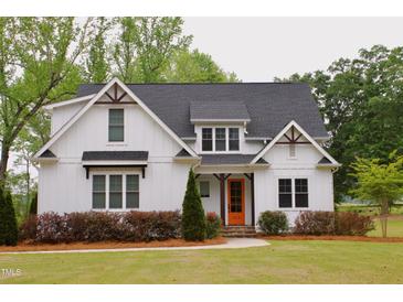 Charming two-story home featuring white siding, a dark roof, an orange front door, and a well-manicured front yard at 212 Lynch Ave, Lillington, NC 27546