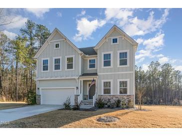 Charming two-story home featuring stone accents, a two-car garage, and a welcoming front porch with an American flag at 25 Courrone, Willow Springs, NC 27592