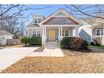 Charming home featuring a welcoming front porch, shingle detailing, a bright yellow front door, and manicured landscaping at 2715 Edmund St, Durham, NC 27705