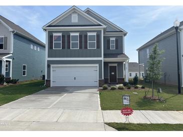 Two-story home featuring a gray exterior, white garage door, and manicured front yard with 'Must See Upgrades' sign at 52 Commons Cir, Clayton, NC 27520