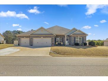 Charming brick home featuring a manicured lawn, a three-car garage, and a welcoming entrance at 99 Preserve Dr, Benson, NC 27504