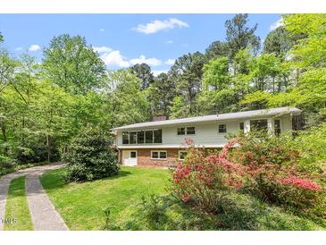 Charming home featuring large windows, brick accents, and lush landscaping, surrounded by mature trees at 703 Caswell Rd, Chapel Hill, NC 27514