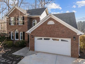 Two-story brick home with a two-car garage and mature landscaping under a partly cloudy sky at 118 N Drawbridge Ln, Cary, NC 27513