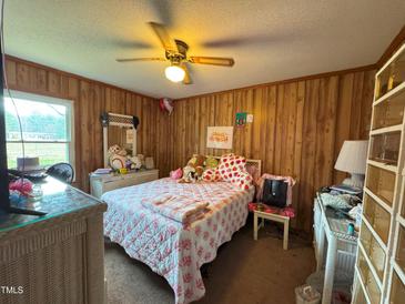 Cozy bedroom features wood paneling, ceiling fan, and bright natural light from a window at 322 Blackstone Rd, Sanford, NC 27330