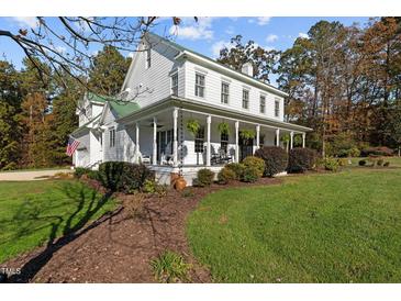 Charming farmhouse-style home featuring a welcoming wrap-around porch and lush landscaped yard at 220 Epps Clark Rd, Siler City, NC 27344