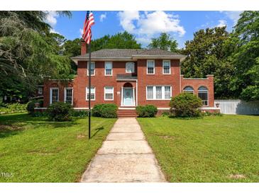 Charming two-story red brick home with landscaped yard and walkway, complemented by an American flag at 1000 S 9Th St, Lillington, NC 27546