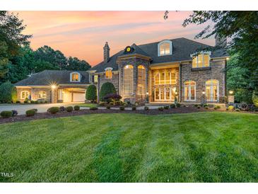 Stunning stone home with a well-manicured lawn and professionally landscaped front yard at sunset at 1801 Oatlands Ct, Wake Forest, NC 27587