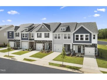 View of new construction townhomes with brick accents and manicured lawns on a sunny day at 64 Lavender Ln, Clayton, NC 27520