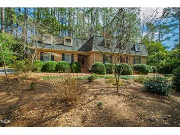 Charming brick home with lush landscaping and dormer windows nestled in a wooded setting at 5008 Hermitage Dr, Raleigh, NC 27612